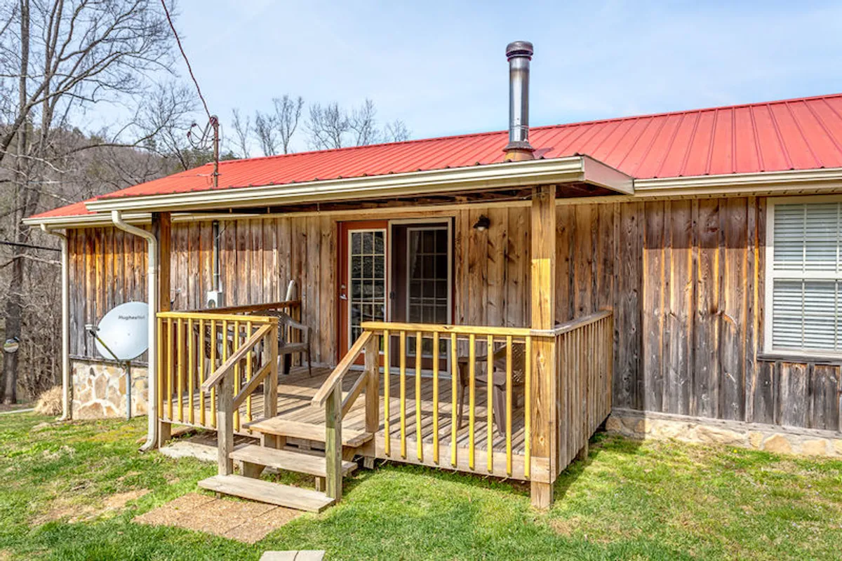 This image highlights the wooden deck and red metal roof, with glass doors opening to the cozy interior. The setting focuses on enjoying sunsets from the porch, gathering around a fire pit, and stargazing, blending the property's outdoor and relaxation features.