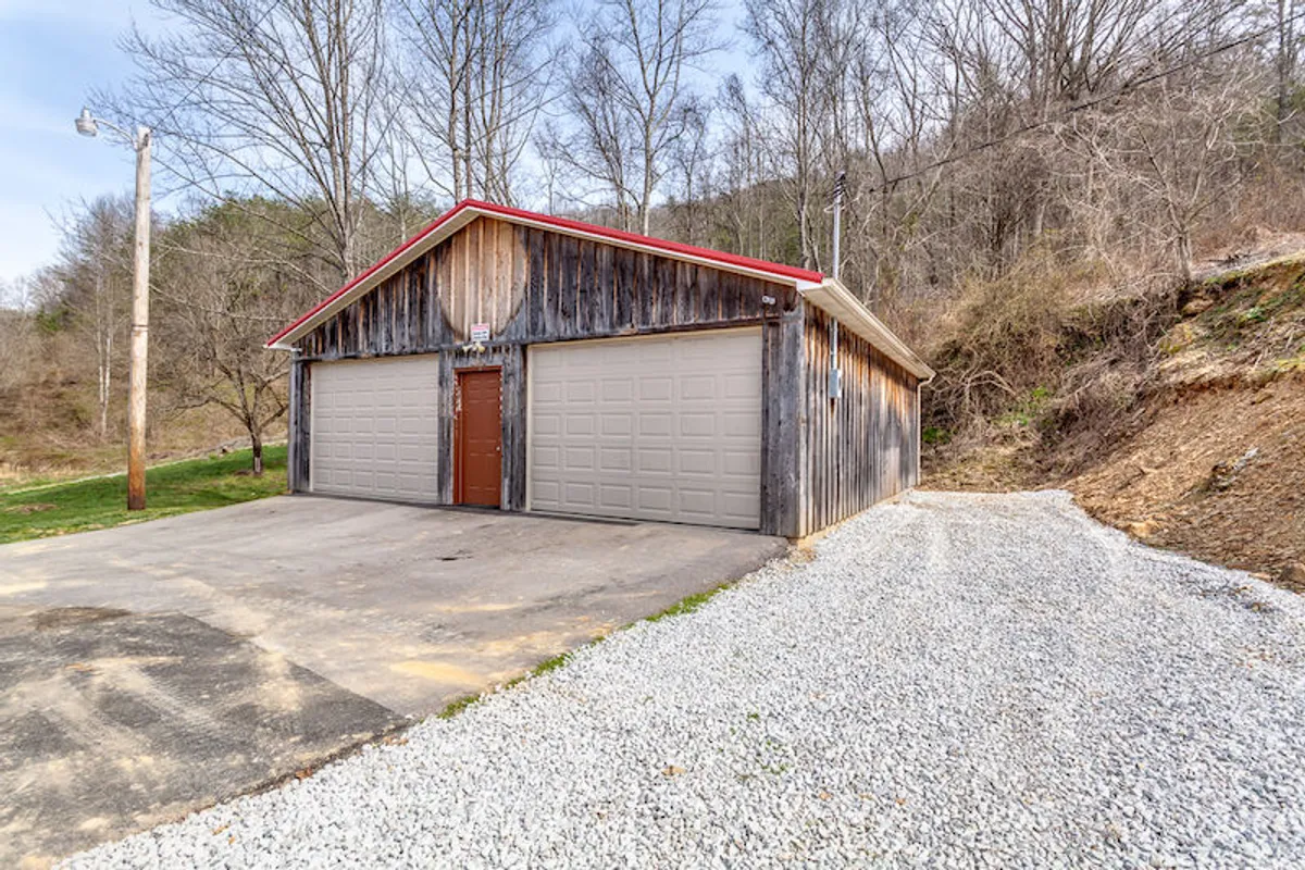 An exterior shot featuring a rustic wooden garage with a red roof and a gravel driveway, surrounded by natural landscaping. The setting evokes a sense of seclusion and peacefulness, with open space for reflection or outdoor activities.
