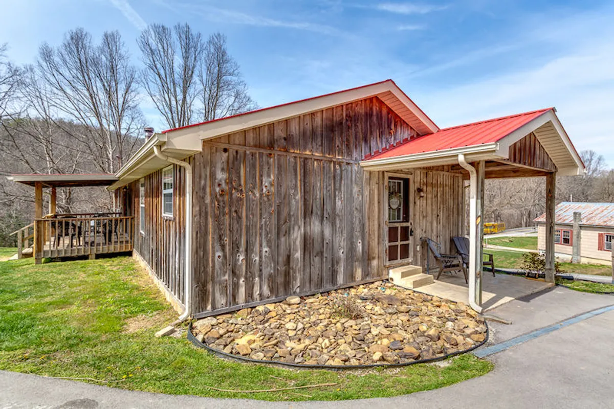 A welcoming exterior shot featuring the home's wooden façade, red roof, stone landscaping, and inviting porch. The scene is set at sunset, with hints of relaxation and social moments on the porch, reinforcing the idea of winding down after an adventurous day.