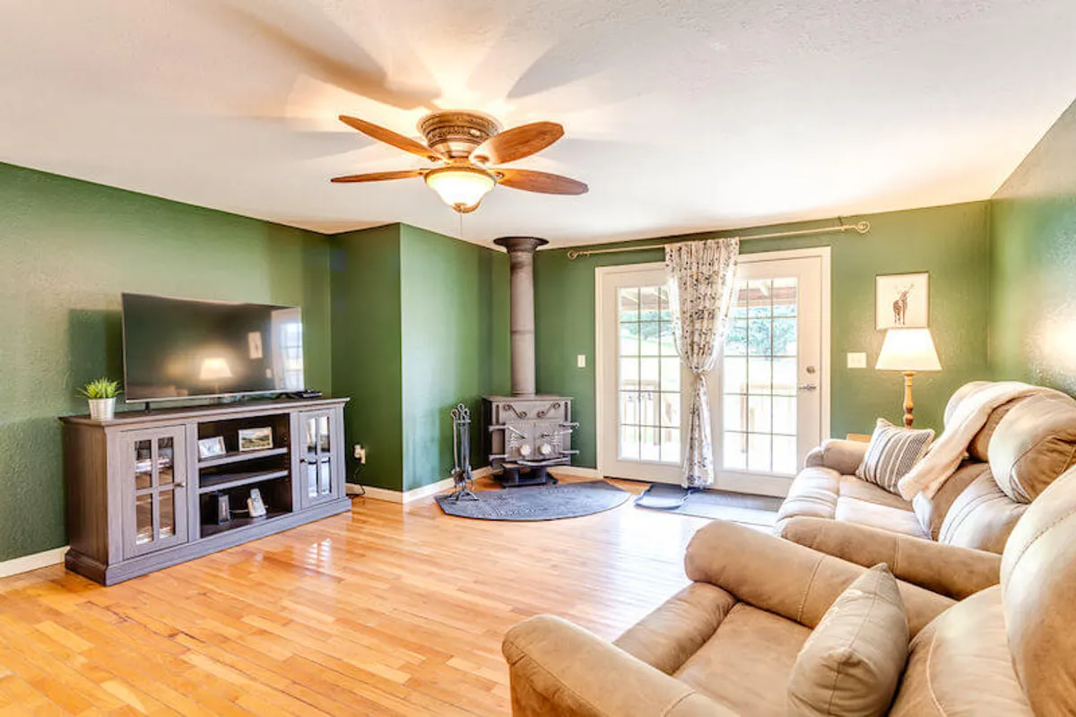 A warm, inviting living room featuring a comfortable sofa facing a wood-burning fireplace with a TV above it. Sunlight filters through the windows with cozy curtains, and board games are stacked on the coffee table, emphasizing a space designed for relaxation and connection after outdoor adventures.