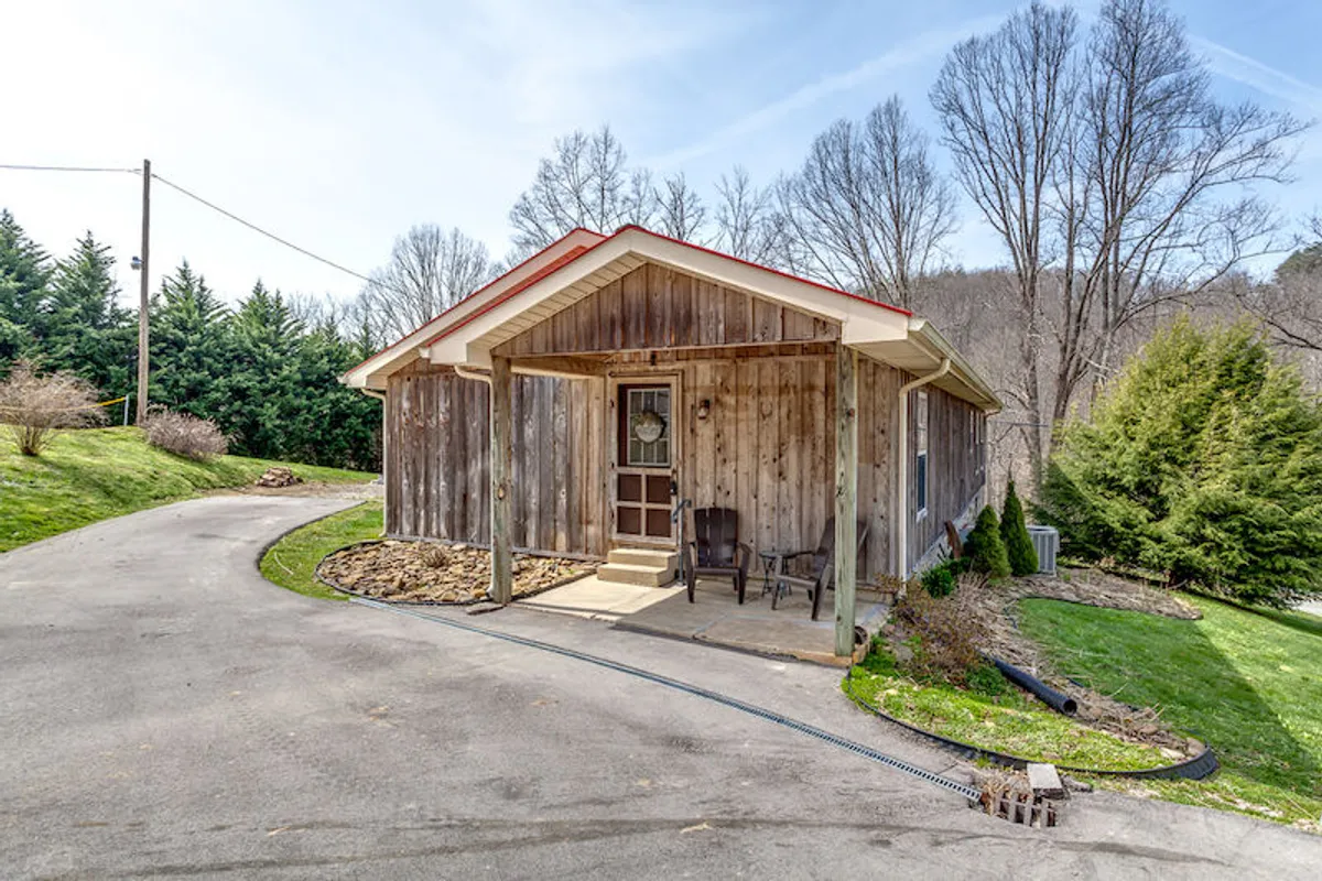 This exterior image showcases the inviting wooden facade of the house, a charming front porch with room for seating, and a landscaped yard surrounded by natural greenery. The porch is perfectly positioned for enjoying the tranquil mountain atmosphere, with morning sunlight bathing the space.