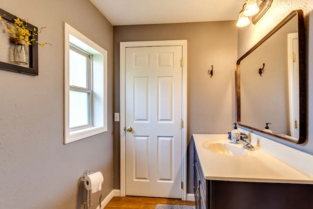 A serene bathroom space with a sleek vanity, framed mirror, and a window streaming with natural light. Thoughtful decorative touches and wall art create an inviting environment for morning and evening routines.