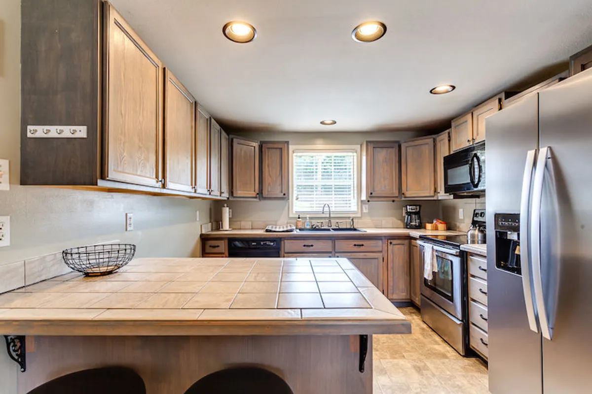A view of a spacious kitchen featuring a central island, stainless steel appliances, and a large window that fills the room with natural light. The kitchen is set up for both everyday meal prep and family gatherings, with ample counter space and modern amenities clearly visible.