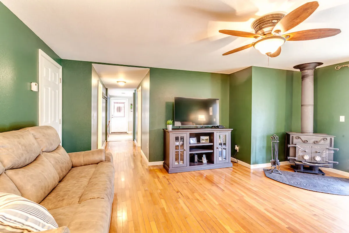 A relaxed living space with a plush sofa, a television set in a cabinet, a wood-burning stove, and a ceiling fan overhead. The arrangement suggests easy conversation, movie nights, and warmth after an outdoor day, with easy access to store or grab gear.