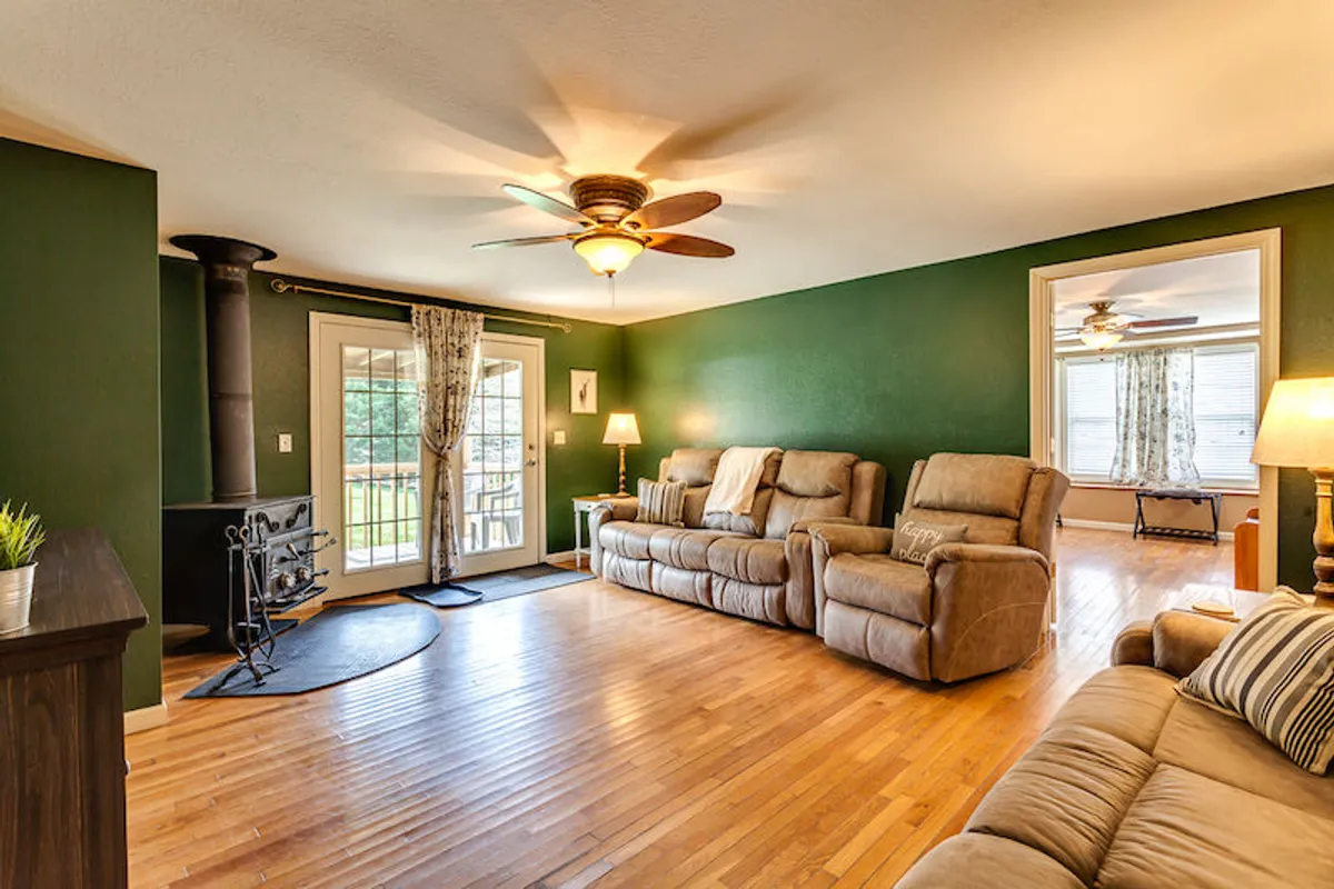 A spacious seating area featuring a wood-burning stove, large windows letting in natural light, and comfortable chairs arranged for both relaxation and socializing. The open sightlines suggest easy flow between living, dining, and kitchen areas, in line with the section's mention of an open layout.